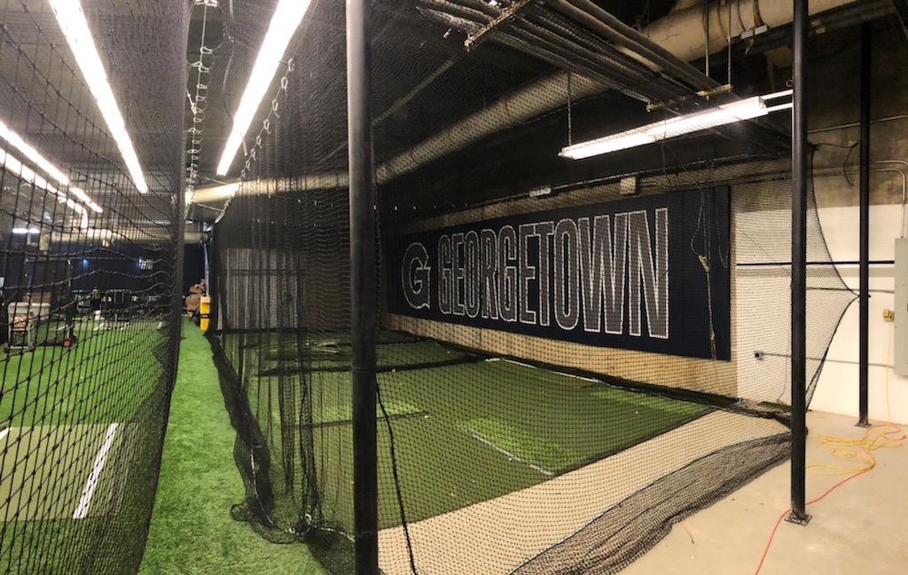 A baseball field with batting cages and grass.