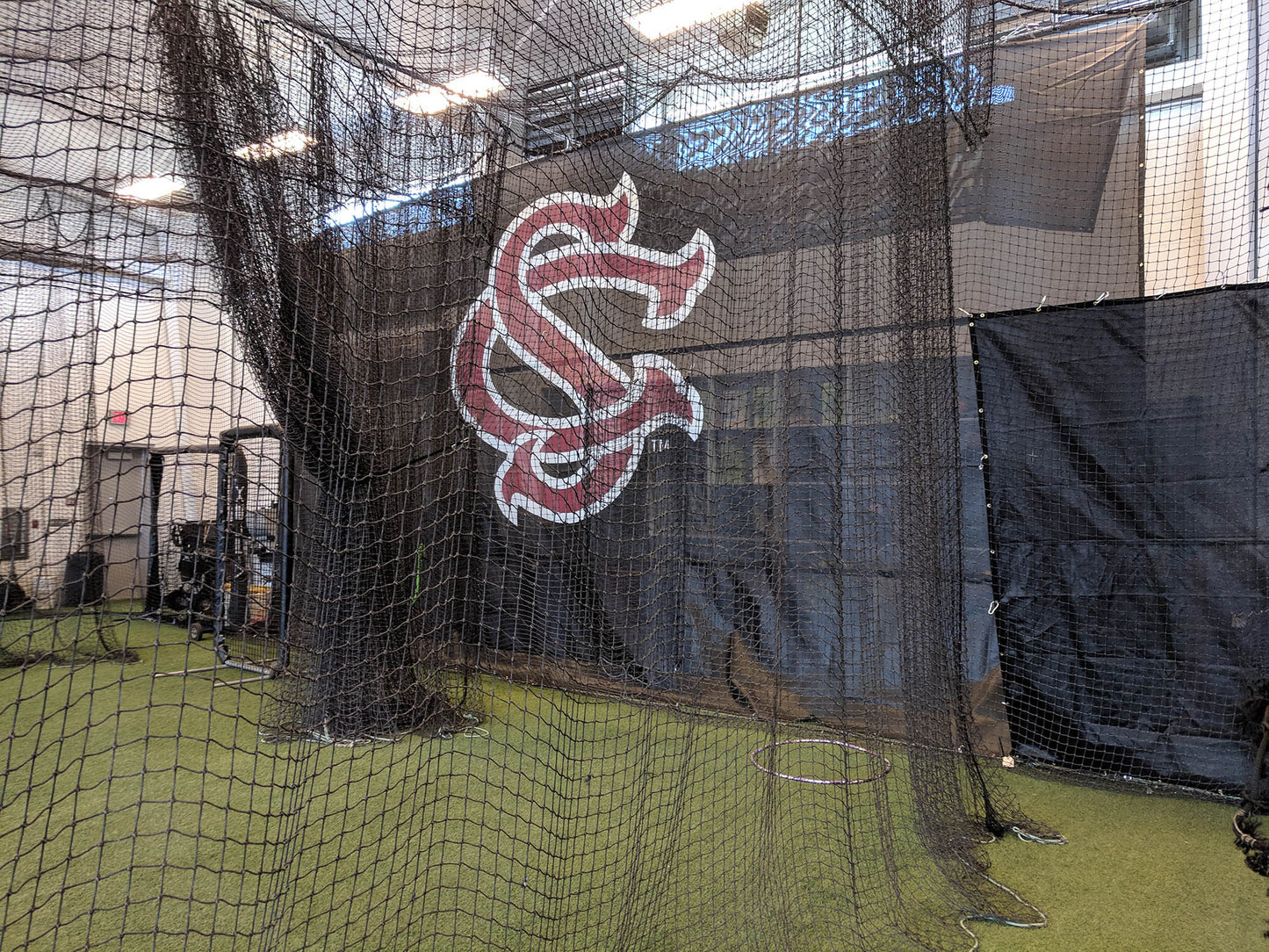 A baseball field with a batting cage and a wall.