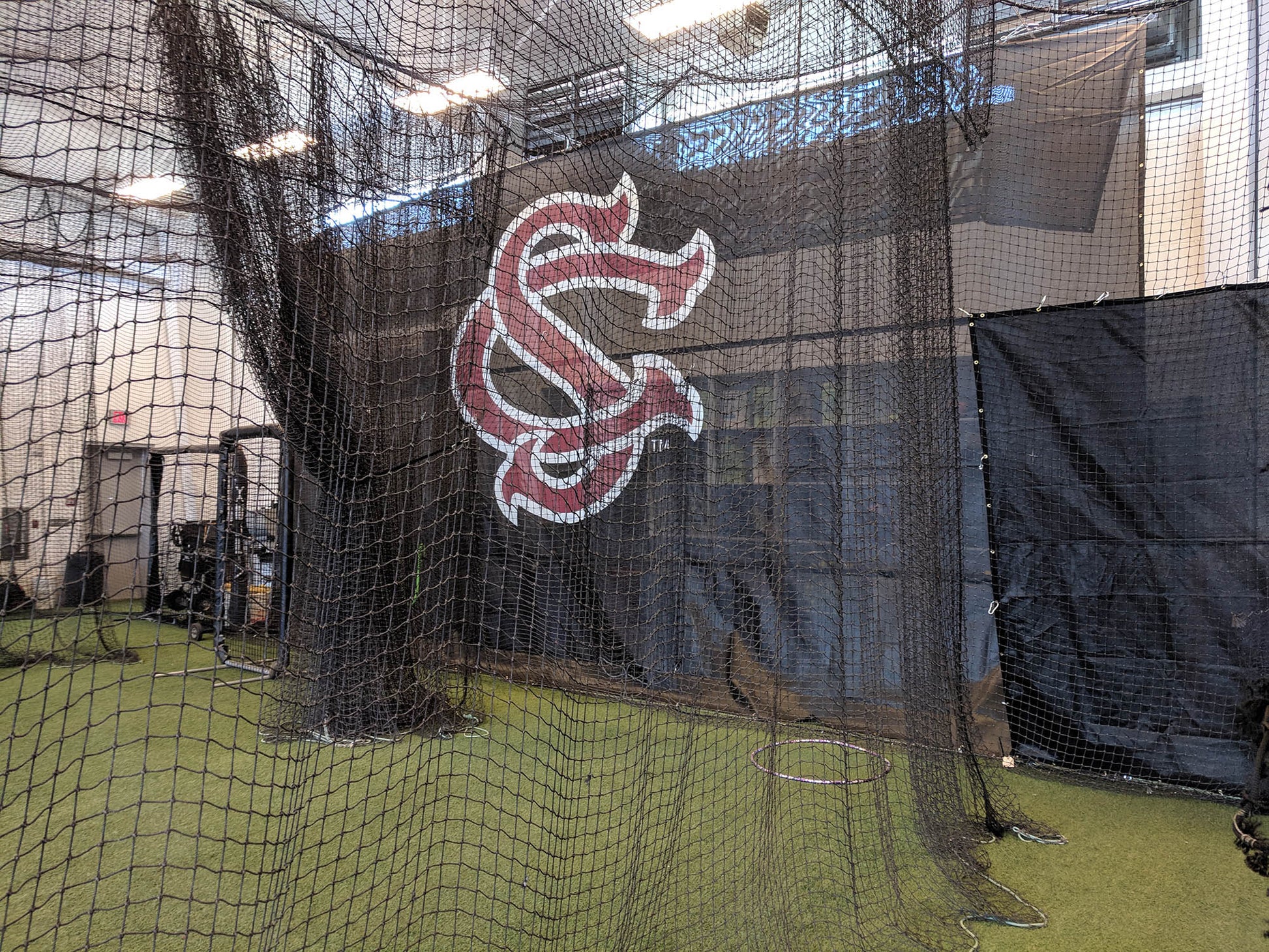 A baseball field with a batting cage and a wall.