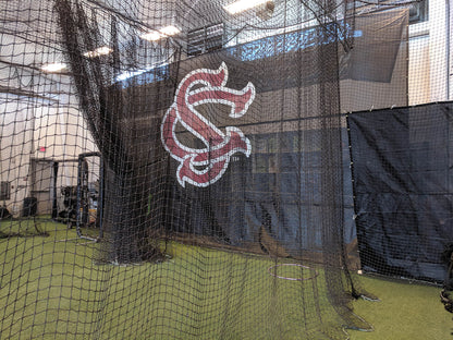 A baseball field with a batting cage and a wall.